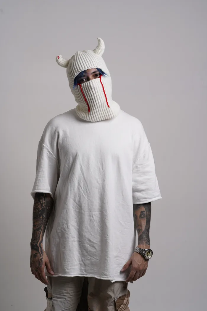 SEVEN77 de face en cagoule à cornes, regardant par l'ouverture, bras le long du corps et tatouages sur les deux avant-bras