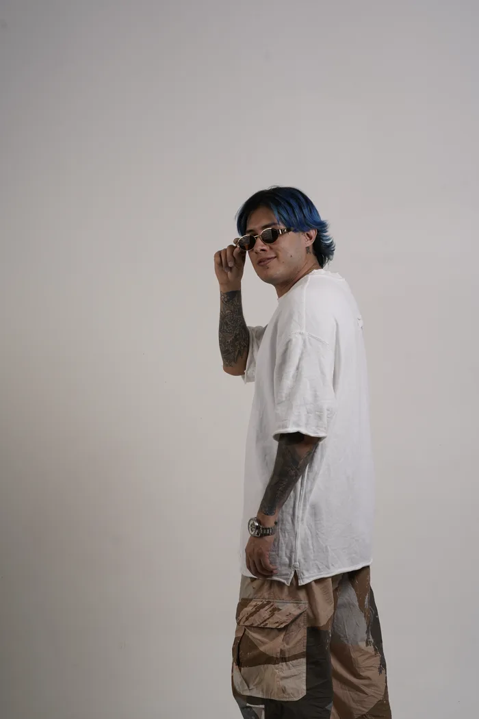 SEVEN77 de profil, ajustant ses lunettes de soleil, en tee-shirt blanc et cargo camouflage