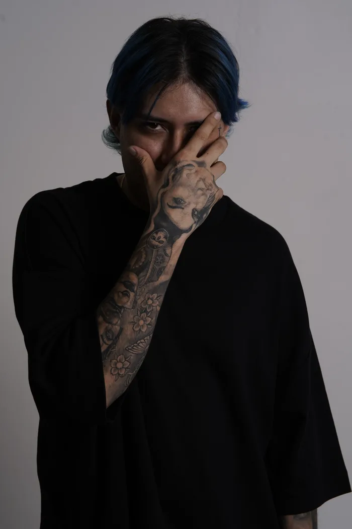 SEVEN77 habillé en noir, la main tatouée couvrant la moitié du visage, un seul œil visible