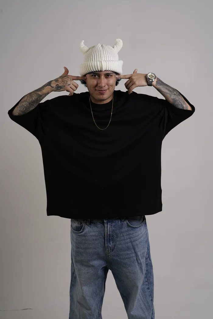 SEVEN77 pointant des deux index les cornes de son bonnet, en tee-shirt noir et jean