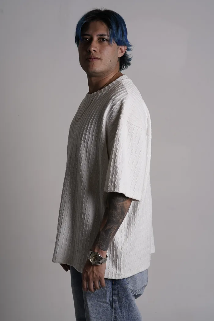 SEVEN77 de profil en tee-shirt blanc texturé et jean, regardant la caméra